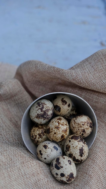 Quail eggs in a bowl on a rustic cloth on a light blue background