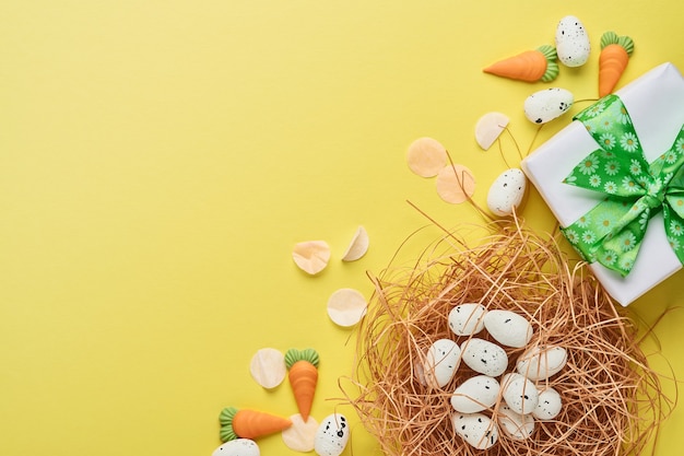 Quail eggs in nest and gift box with green ribbon on yellow trend color table. Easter minimal creative horizontal composition with copy space. Spring Happy Easter holiday card. Top view.