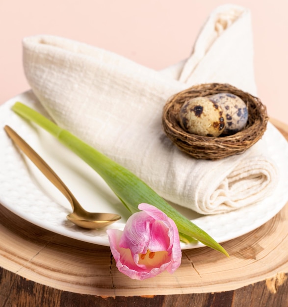 Quail eggs on rolled as bunny ears cotton napkin white plate golden spoon tulip on wooden stand