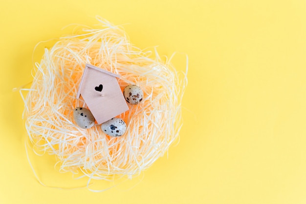 Photo quail eggs in a straw nest, wooden bird feeder on a yellow background.  easter concept.