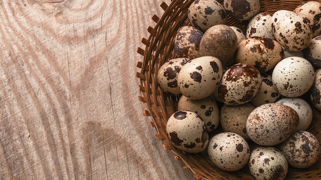 Quail eggs in wicker basket on wooden background