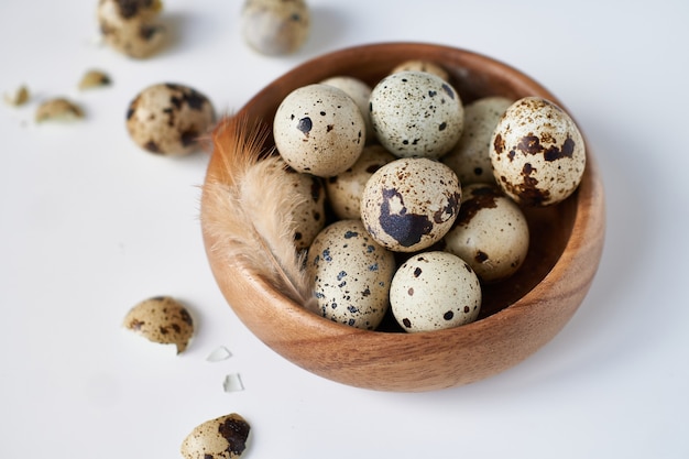 Quail eggs in a wooden bowl painted with a feather on a white table. Easter concept Copy space