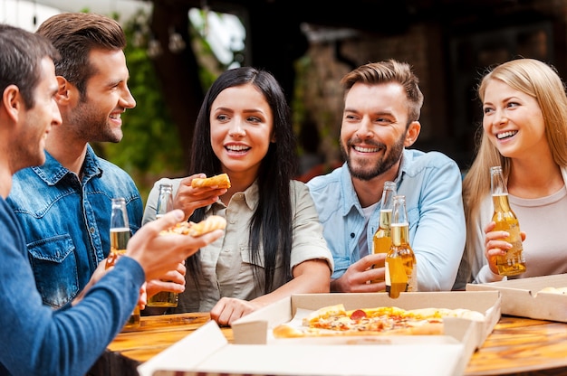 Quality time with friends. Group of happy young people eating pizza and drinking beer while standing outdoors