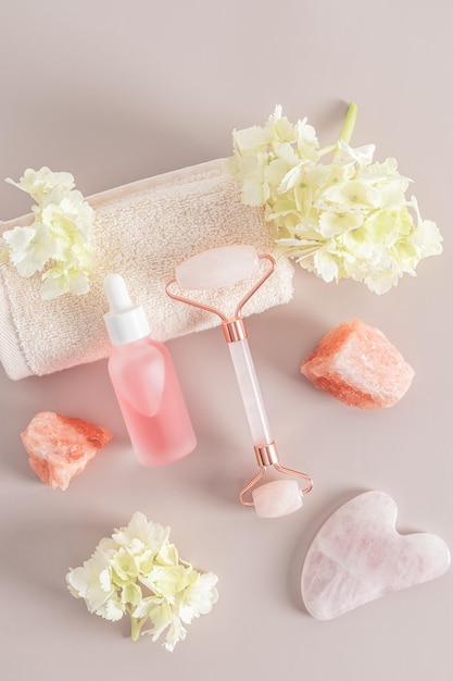 Quartz roller massager gua sha matte bottle with a cosmetic product for maasage and face and body skin care Vertical view hydrangea flowers