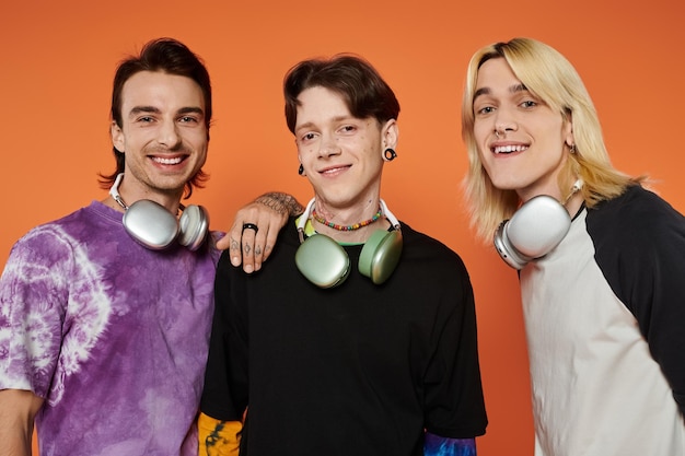 Photo queer friends pose with headphones against orange background