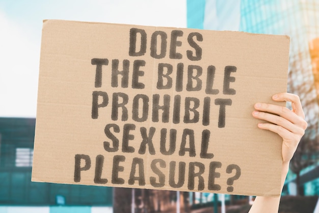 The question Does the Bible prohibit sexual pleasure is on a banner in men's hands with blurred background Sexual Ecstasy Girlfriend Intimacy Erotic Evil Figure Sin Biblical Christ Bed