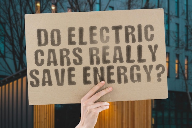 The question Do electric cars really save energy is on a banner in men's hands with blurred background Vehicle Battery Electric Alternative Fuel Power Energy Cable Transport Hybrid