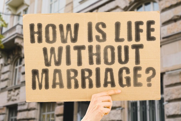 The question How is life without marriage is on a banner in men's hands with blurred background Female Married Smile Bride Smiling Family Young Girlfriend Lady Romantic Boyfriend