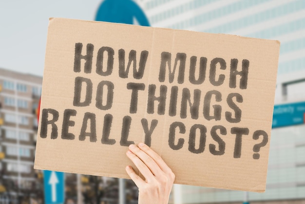 The question How Much Do Things Really Cost is on a banner in men's hands with blurred background Retail Rising Sale Saving Success Tag Valuable Value Wealth Price Product