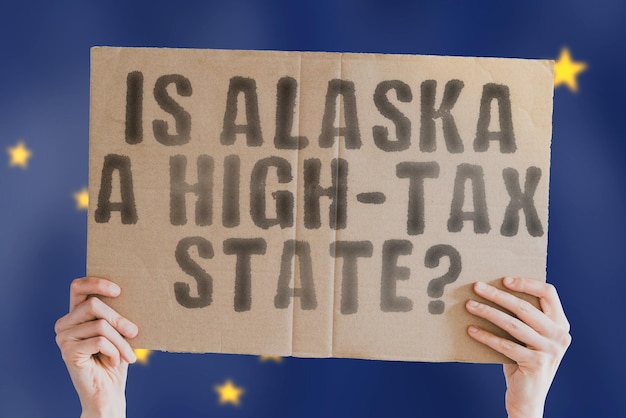 The question Is Alaska a hightax state is on a banner in men's hands with blurred background Cost Budget Crisis Decision Earnings Freedom Interest Revenue