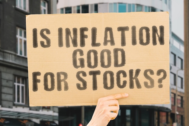 The question " Is inflation good for stocks? " on a banner in men's hand with blurred background. Deposit. Achievement. Bubble. Bankruptcy. Credit. Despair. Commercial. Earning. Failure. Emergency