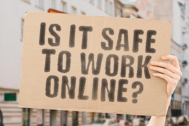 The question Is it safe to work online is on a banner in men's hands with blurred background Web Data Digital Laptop Safe Shield Safeguard Guard Worker Service Social Busy