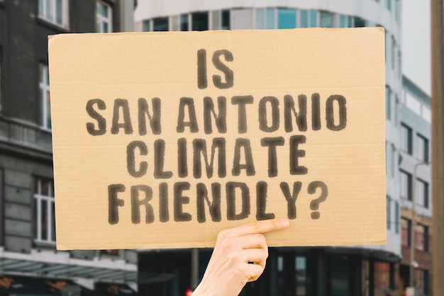 The question Is San Antonio climatefriendly is on a banner in men's hands with blurred background Support Team Activist Urban Sunset Carbon Ecology Energy New Clean Warming Waste