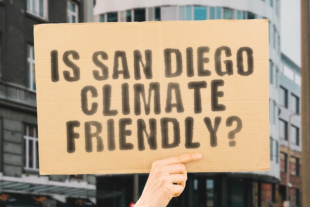 The question Is San Diego climatefriendly is on a banner in men's hands with blurred background Support Team Activist Urban Sunset Carbon Ecology Energy New Clean Warming Waste