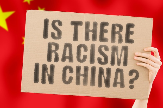 The question Is there racism in China is on a banner in men's hands with a blurred Chinese flag in the background Interracial Issues Justice Nation Politics Peace Patriotism Rebellion