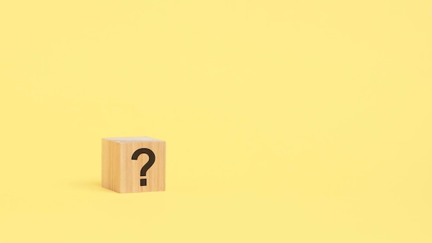 Question mark drawn on wooden block over yellow background with copy space