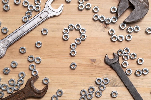 Question mark made of metal nuts on a wooden table a variety of wrenches lie nearby