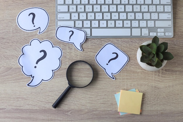 Question mark, magnifying glass and keyboard on office desk. FAQ concept. Working with clients.