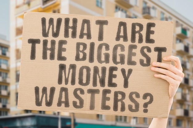 The question What are the biggest money wasters is on a banner in men's hands with blurred background Inflation Bank Expense Idea Management Garbage Rubbish Throwing Risk Lost Growth