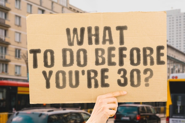 The question What to do before you're 30 on a banner in men's hand with blurred background Skill Plan Target Option Rich Goal Vision Genius Good Future Comfort Age Happy Smart