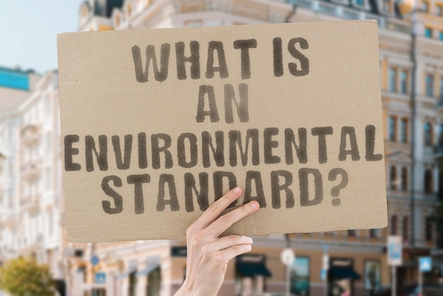 The question What is an environmental standard is on a banner in men's hands with blurred background Protect Manufacturing Procedure Risk Security Social Production Sustainability