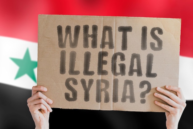 The question " What is illegal in Syria? " on a banner in men's hand with blurred Syrian flag on the background. Not allowed. Prohibitions. Outlaw. Rules. Policy. Law