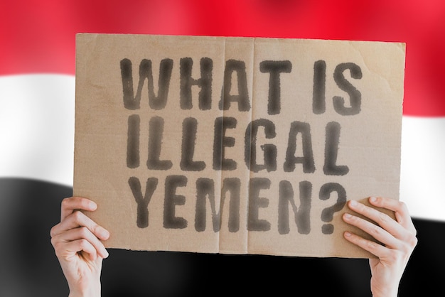 The question " What is illegal in Yemen? " on a banner in men's hand with blurred Yemeni flag on the background. Not allowed. Prohibitions. Outlaw. Rules. Policy. Law