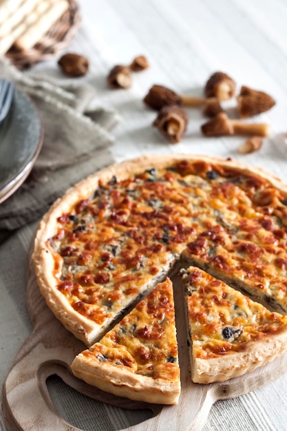 Quiche open tart pie with morel mushrooms onion and cheese on wooden cutting board