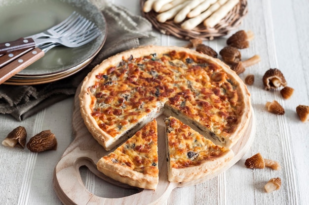 Quiche open tart pie with morel mushrooms onion and cheese on wooden cutting board