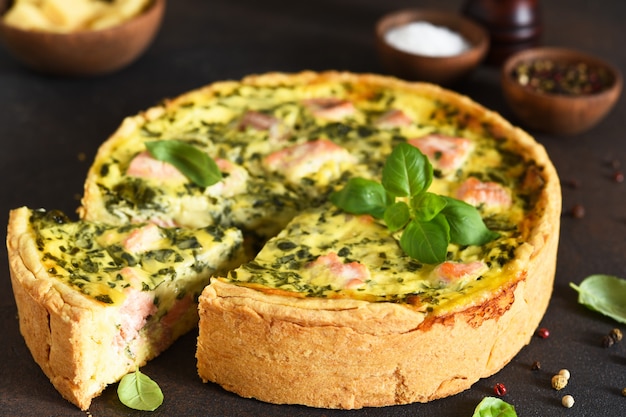 Quiche (pie) with salmon, spinach and soft cheese on a dark concrete.