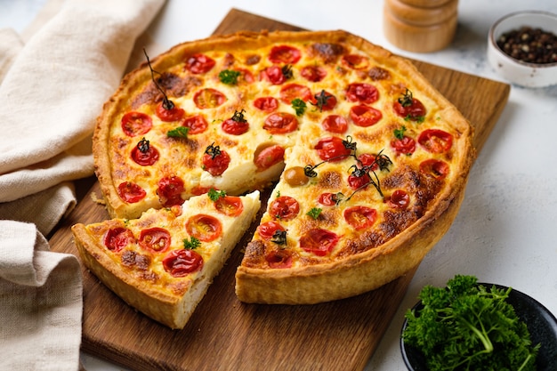 Quiche with chicken, cherry tomatoes and cheese. Appetizing open French pie. Dish on a wooden board on the kitchen table. Horizontally.