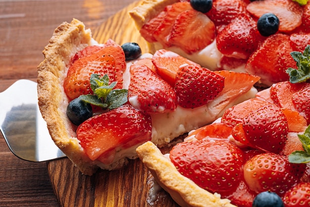 Quiche with lime zest on which sliced strawberries with blueberries and fresh mint leaves on a wooden table one slice is cut out of the pie and it is ready to serve