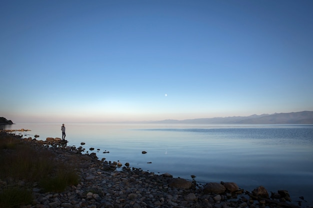 Quiet sunset over the river. The girl stands on the rocky shore.