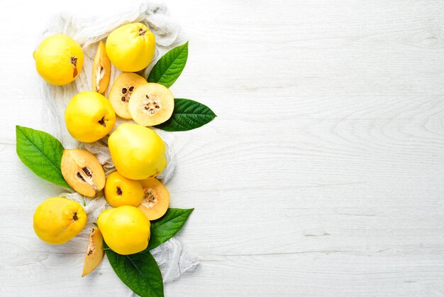 Quince fruits with leaves on white wooden background.