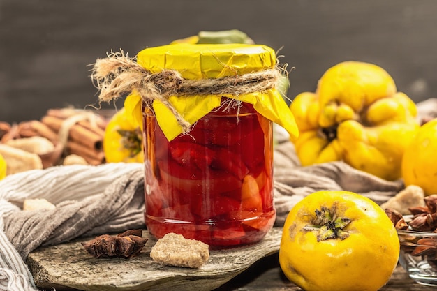 Quince jam or confiture brewed with brown sugar. Ripe whole fruits, sweet dessert, fragrant spices. Trendy wooden stand, old boards background, close up