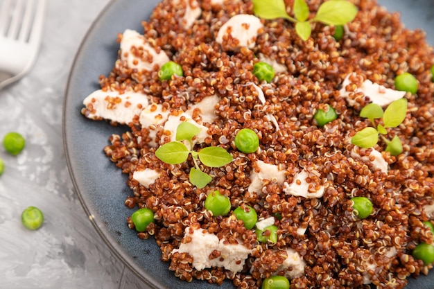 Quinoa porridge with green pea and chicken on ceramic plate on a gray concrete background and orange textile. Top view, close up, selective focus.