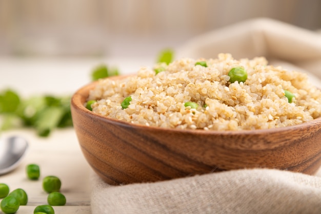 Quinoa porridge with green pea in wooden bowl on a white wooden background. Side view, selective focus.