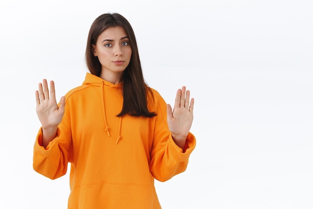 Quit it end now Skeptical and reluctant seriouslooking bossy woman in orange hoodie raise hands to show stop gesture refuse express disapproval disagree with person during conversation