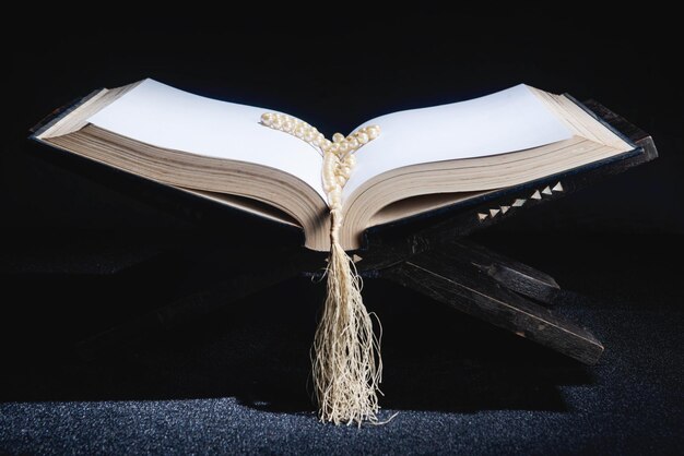 Quran open on a wooden placemat with prayer beads on the dark background