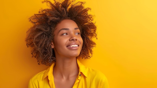 Radiant young woman with beautiful afro hair smiling against a monochrome yellow background portrait