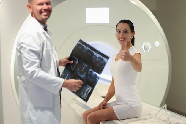 Radiologist holds mri scans results while standing near ct scanner and patient female patient