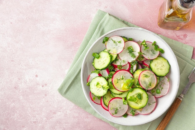 Radish salad with cucumber dill onion and olive oil in a plate with fork on pink concrete background Top view