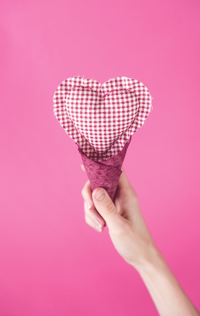 Rag heart in a waffle cup in a hand on a pink background