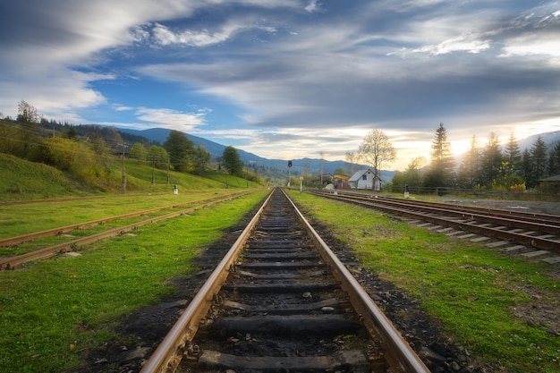 Railroad in mountains at sunset in summer Beautiful industrial landscape with railway station trees green grass blue sky clouds in spring Old rural railway platform in Ukraine Transportation