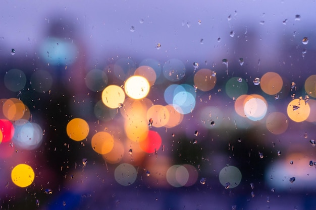 Rain drops in blue glass background City street lights bokeh defocused abstract dusk night city background