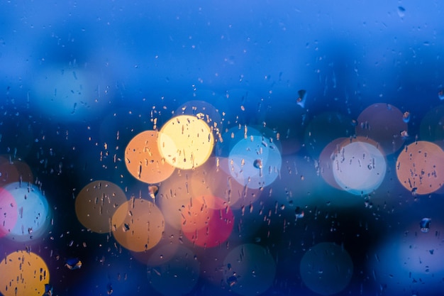 Rain drops in blue glass background City street lights bokeh defocused abstract dusk night city background