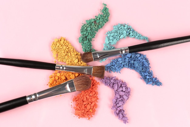 Rainbow crushed eyeshadow and professional make-up brush on pink surface