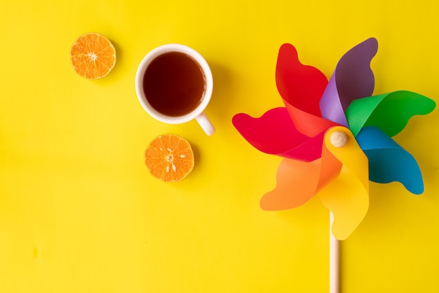 Rainbow pinwheel on yellow with hot drink and sliced orange fruit flat lay