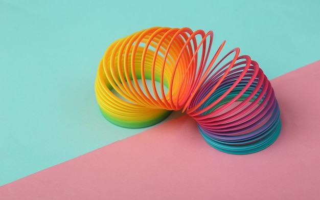 Rainbow plastic multicolored spiral slinky toy on pink blue background