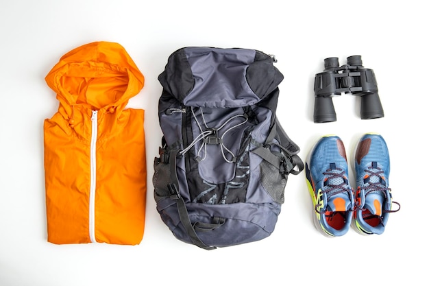 Raincoat backpack sneakers binoculars on a white background Top view flat lay